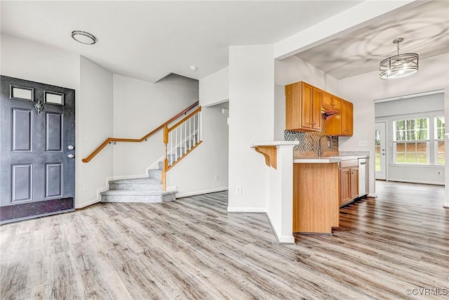 kitchen featuring baseboards, stainless steel dishwasher, light wood finished floors, and light countertops
