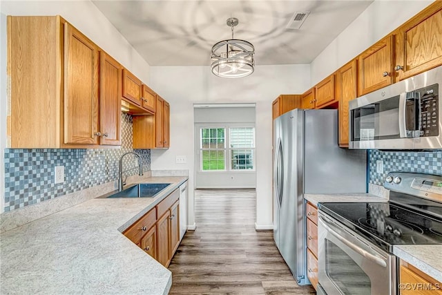 kitchen with wood finished floors, a sink, appliances with stainless steel finishes, a notable chandelier, and visible vents