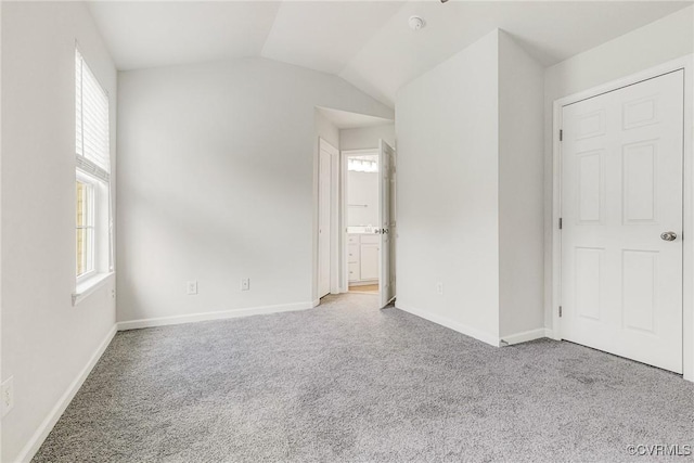 unfurnished bedroom with carpet floors, lofted ceiling, baseboards, and connected bathroom