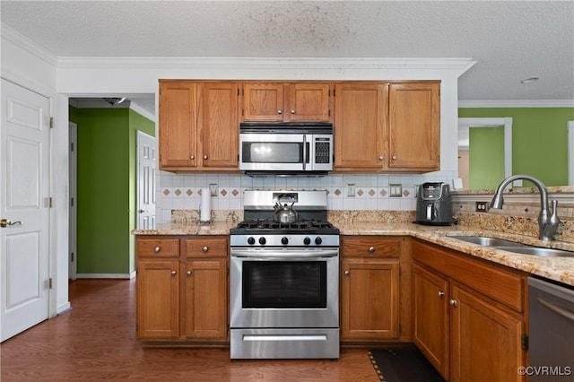 kitchen with a sink, appliances with stainless steel finishes, brown cabinets, and ornamental molding