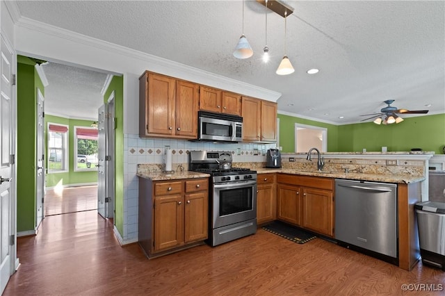 kitchen featuring dark wood-style flooring, a peninsula, brown cabinets, a sink, and stainless steel appliances