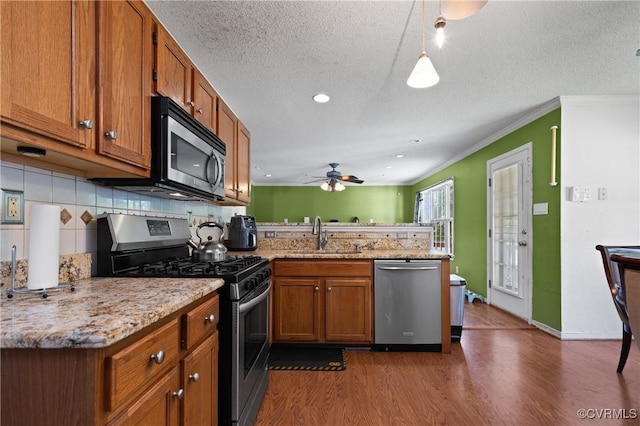 kitchen featuring a peninsula, appliances with stainless steel finishes, brown cabinetry, and a sink
