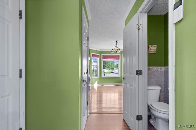 bathroom featuring a textured ceiling, tile walls, a wainscoted wall, toilet, and ornamental molding