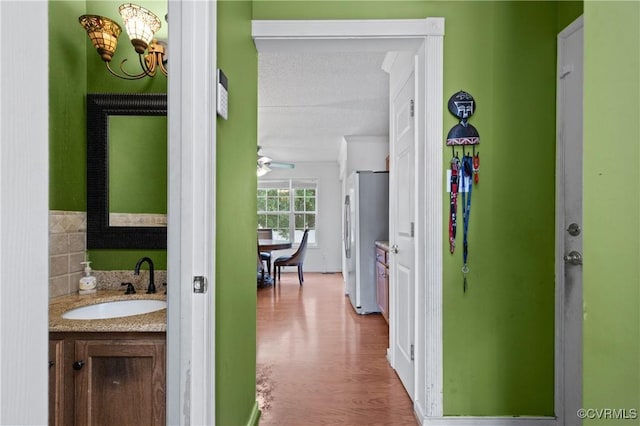 hallway with a sink, a textured ceiling, wood finished floors, and a notable chandelier