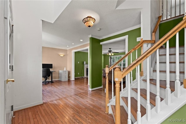 stairs with ceiling fan, crown molding, a fireplace, baseboards, and hardwood / wood-style floors