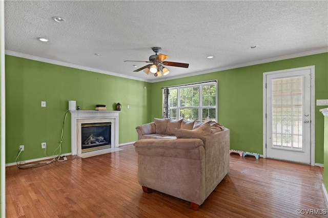 living area featuring a ceiling fan, ornamental molding, wood finished floors, a textured ceiling, and a fireplace with flush hearth
