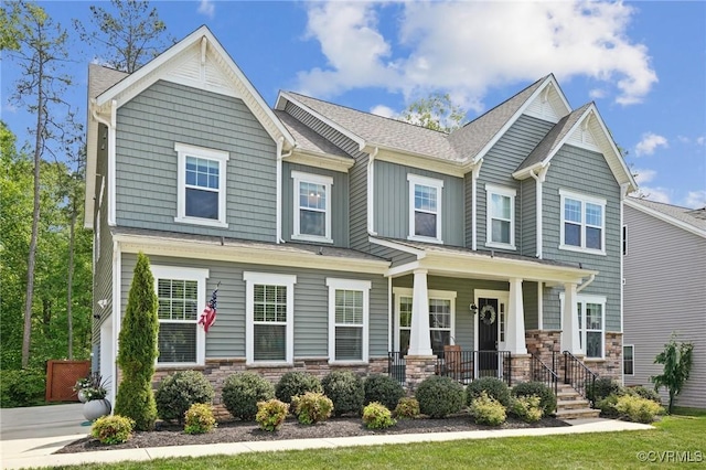 craftsman house with stone siding, a porch, and a shingled roof