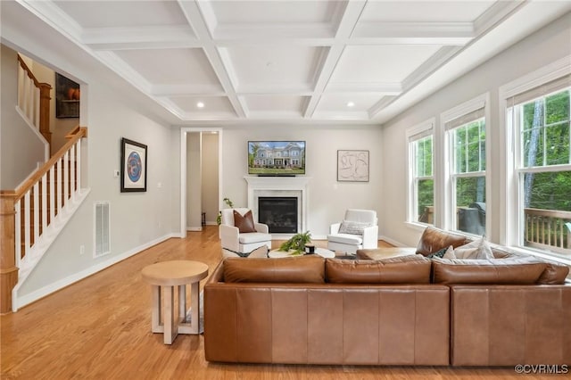 living area with beam ceiling, visible vents, stairway, a glass covered fireplace, and light wood-style floors
