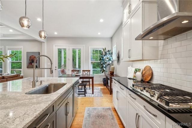 kitchen featuring a sink, light wood-type flooring, wall chimney range hood, and pendant lighting