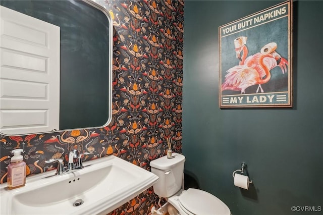bathroom featuring wallpapered walls, toilet, and a sink