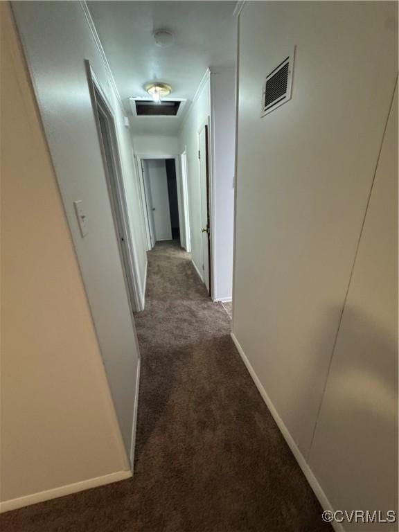 hall with baseboards, visible vents, and dark carpet