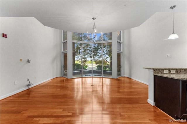 unfurnished dining area featuring a towering ceiling, wood finished floors, a wall of windows, baseboards, and a notable chandelier