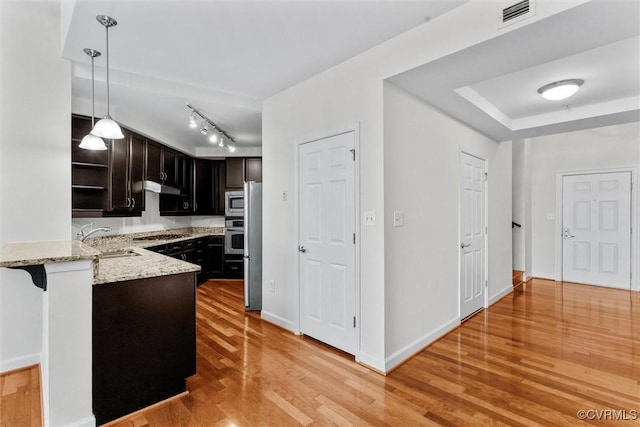 kitchen featuring light stone counters, a sink, light wood-style flooring, appliances with stainless steel finishes, and visible vents
