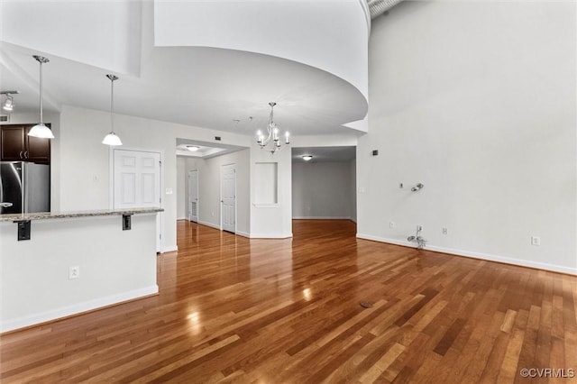 unfurnished living room featuring a chandelier, wood finished floors, and baseboards