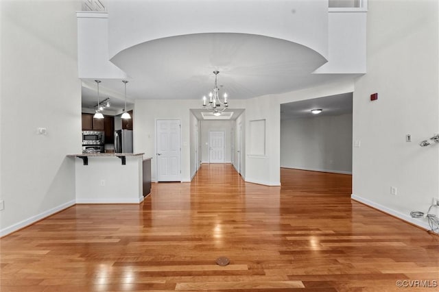 unfurnished dining area featuring arched walkways, an inviting chandelier, light wood finished floors, and baseboards