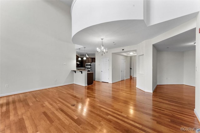 unfurnished living room featuring light wood finished floors, baseboards, and a chandelier