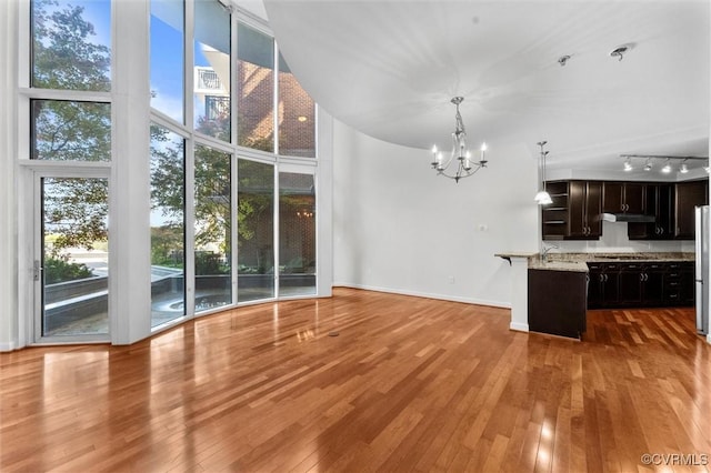 unfurnished living room featuring light wood finished floors, a sink, baseboards, a notable chandelier, and a high ceiling