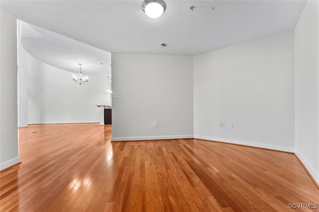 spare room featuring light wood-style flooring, baseboards, and a chandelier