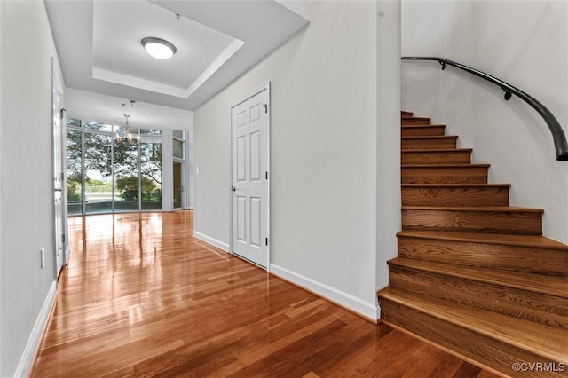 stairs featuring a tray ceiling, baseboards, a notable chandelier, floor to ceiling windows, and wood finished floors
