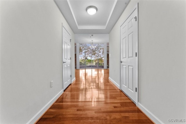 hall featuring baseboards, wood finished floors, an inviting chandelier, and a raised ceiling