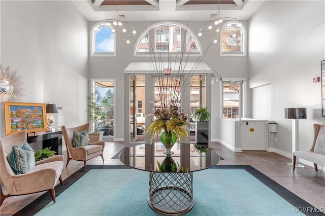 living area with baseboards, a notable chandelier, a towering ceiling, and tile patterned floors