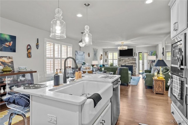 kitchen with wood finished floors, a kitchen island with sink, a fireplace, white cabinets, and appliances with stainless steel finishes