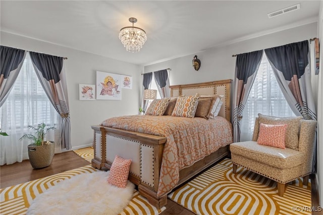 bedroom featuring baseboards, visible vents, wood finished floors, and a chandelier