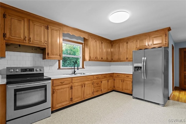 kitchen featuring backsplash, appliances with stainless steel finishes, brown cabinets, a sink, and light countertops