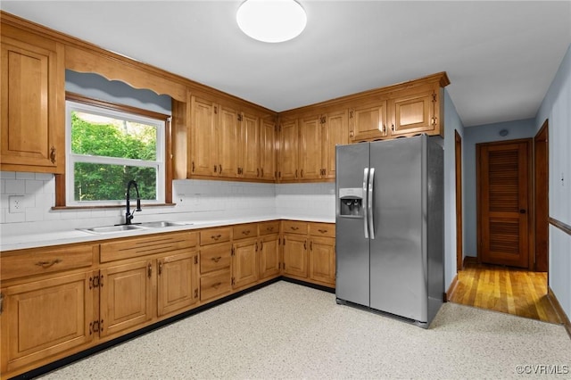 kitchen with backsplash, stainless steel fridge, a sink, and light countertops