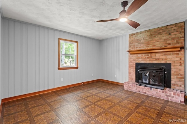 unfurnished living room with ceiling fan, a brick fireplace, a textured ceiling, baseboards, and visible vents