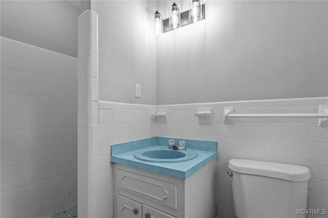 full bathroom with vanity, toilet, tile walls, tiled shower, and a wainscoted wall