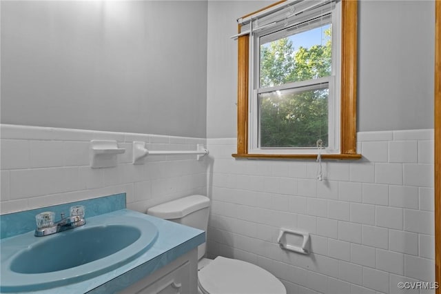 bathroom featuring vanity, a wainscoted wall, toilet, and tile walls