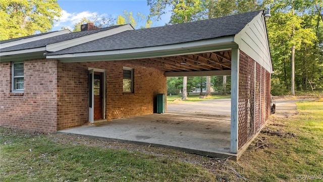view of home's exterior featuring brick siding, roof with shingles, a chimney, and a carport