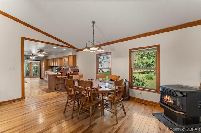 dining room featuring light wood finished floors, vaulted ceiling, baseboards, crown molding, and a wood stove