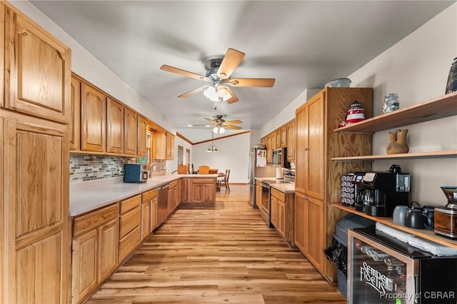 kitchen with light wood finished floors, stainless steel appliances, a peninsula, ceiling fan, and light countertops