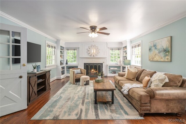 living area featuring crown molding, a ceiling fan, dark wood finished floors, and a lit fireplace