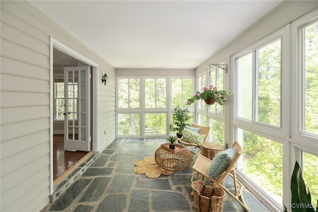 sunroom featuring a healthy amount of sunlight, stone floors, french doors, and wood walls