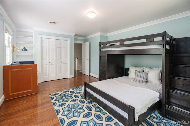 bedroom featuring visible vents, crown molding, wood finished floors, baseboards, and a closet