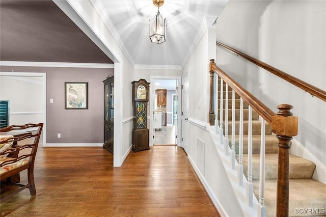 entryway with wood finished floors, ornamental molding, stairs, and baseboards