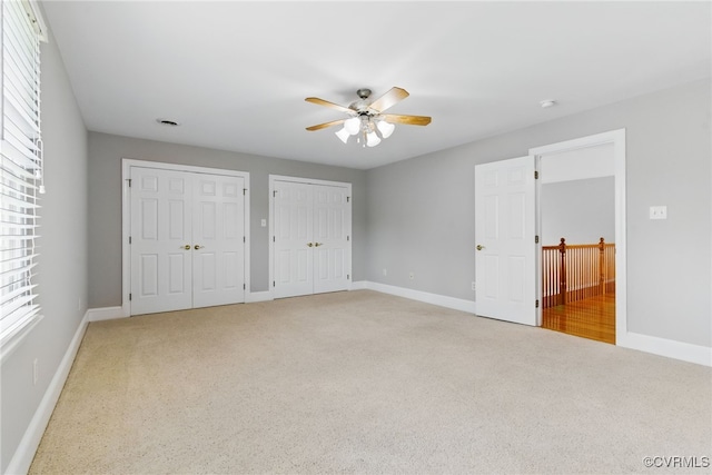 unfurnished bedroom with light colored carpet, baseboards, and two closets