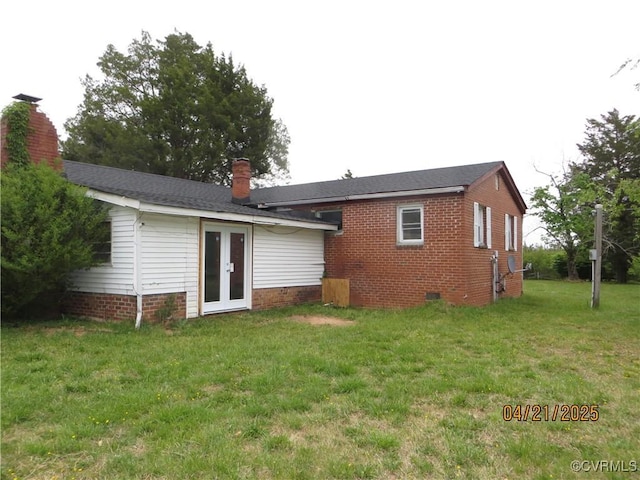 rear view of house with brick siding, a yard, french doors, and a chimney
