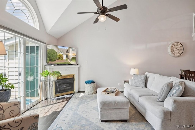 living room with a ceiling fan, high vaulted ceiling, a glass covered fireplace, and a wealth of natural light