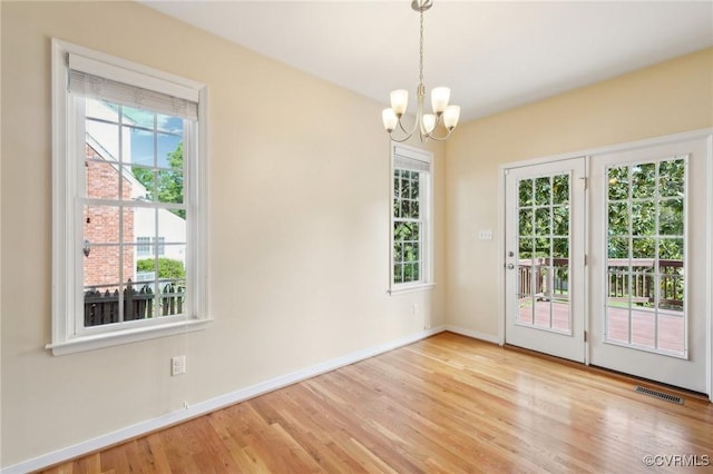 unfurnished dining area with wood finished floors, visible vents, baseboards, and an inviting chandelier