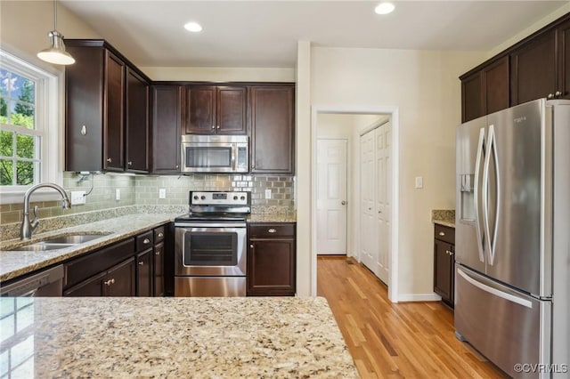 kitchen featuring light stone counters, stainless steel appliances, dark brown cabinets, a sink, and light wood-type flooring