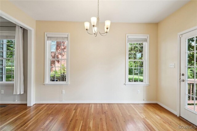 unfurnished dining area with baseboards, wood finished floors, and an inviting chandelier