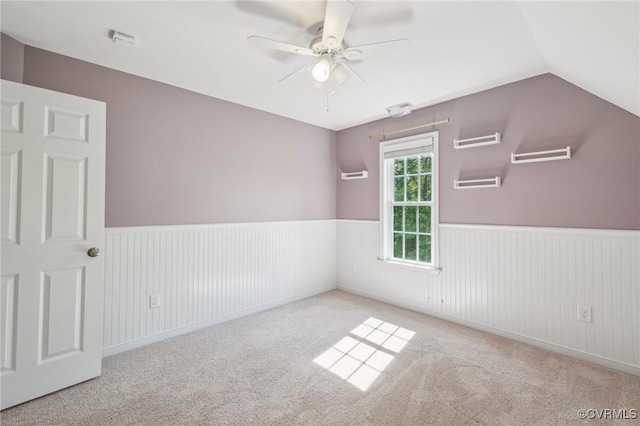 carpeted spare room featuring lofted ceiling, a wainscoted wall, and ceiling fan