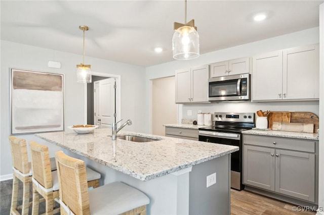kitchen with light stone counters, stainless steel appliances, wood finished floors, a sink, and a center island with sink