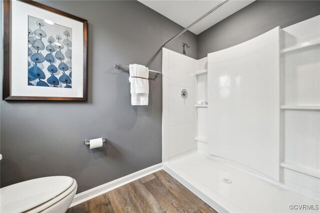 bathroom featuring toilet, wood finished floors, a shower, and baseboards