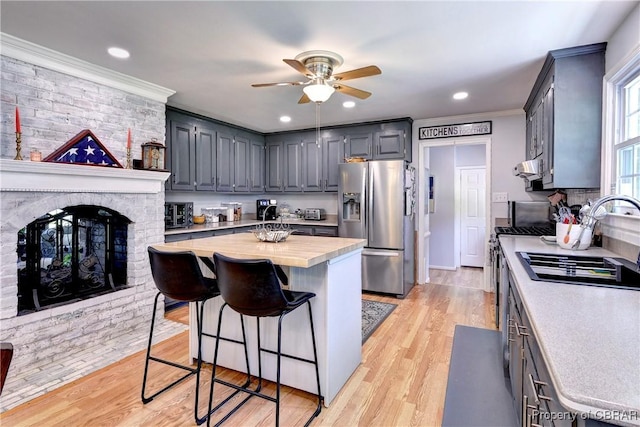 kitchen with a ceiling fan, crown molding, a sink, stainless steel fridge with ice dispenser, and a kitchen island