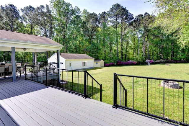 wooden deck featuring an outdoor structure, a yard, a ceiling fan, and a storage unit